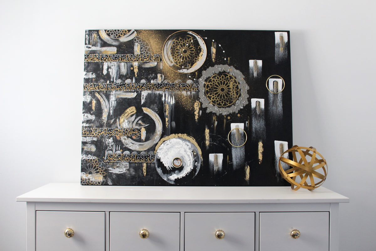 Night Prayer original Islamic painting by Saleha: gold Ayatul Kursi calligraphy and moon phases on a black and white canvas, on a white sideboard