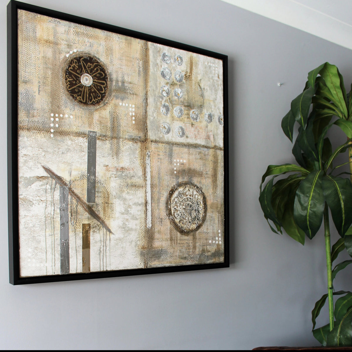 Pilgrimage original Hajj painting by Saleha: silver, gold and grey canvas with Talbiyah calligraphy, framed on a wall beside a plant